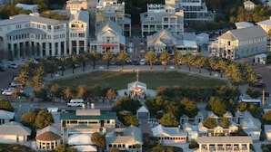 An aerial view of a coastal residential area with multiple houses, a central gazebo, and a beach in the foreground.