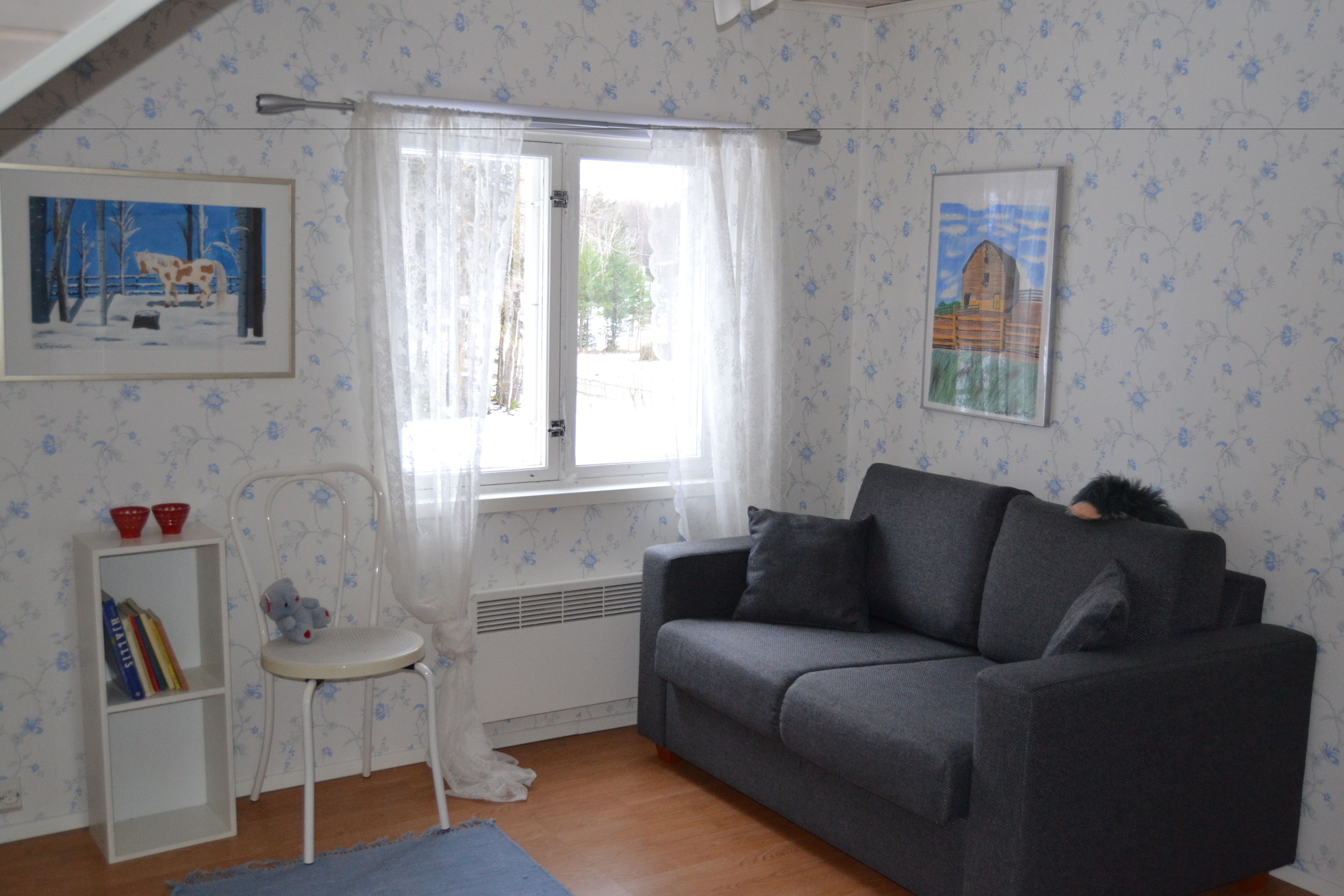 Une pièce chaleureuse avec un canapé gris, une chaise blanche, une petite bibliothèque et deux tableaux encadrés accrochés au mur.