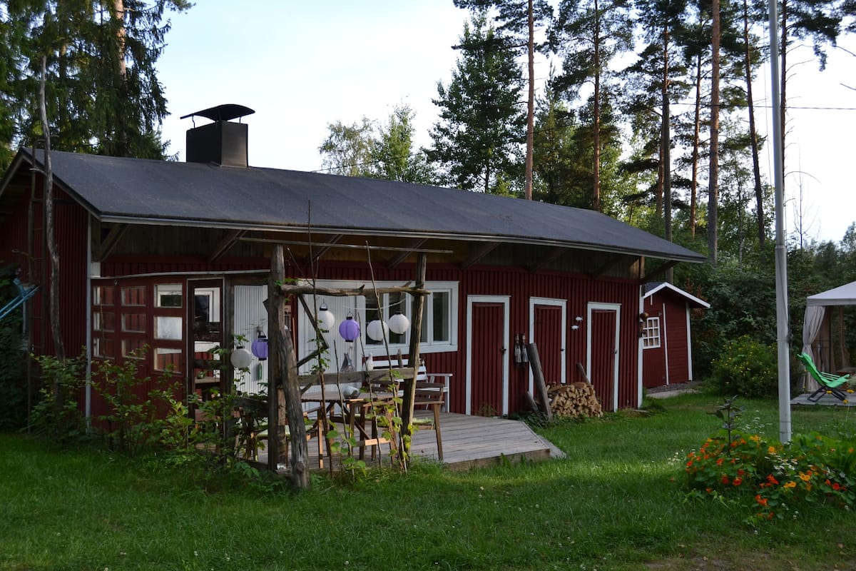A red wooden house with a porch, a chimney, and a garden with flowers.