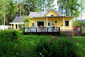 A yellow house with a porch, surrounded by a garden with various flowers. - Majatalo Torppa (Kotka)