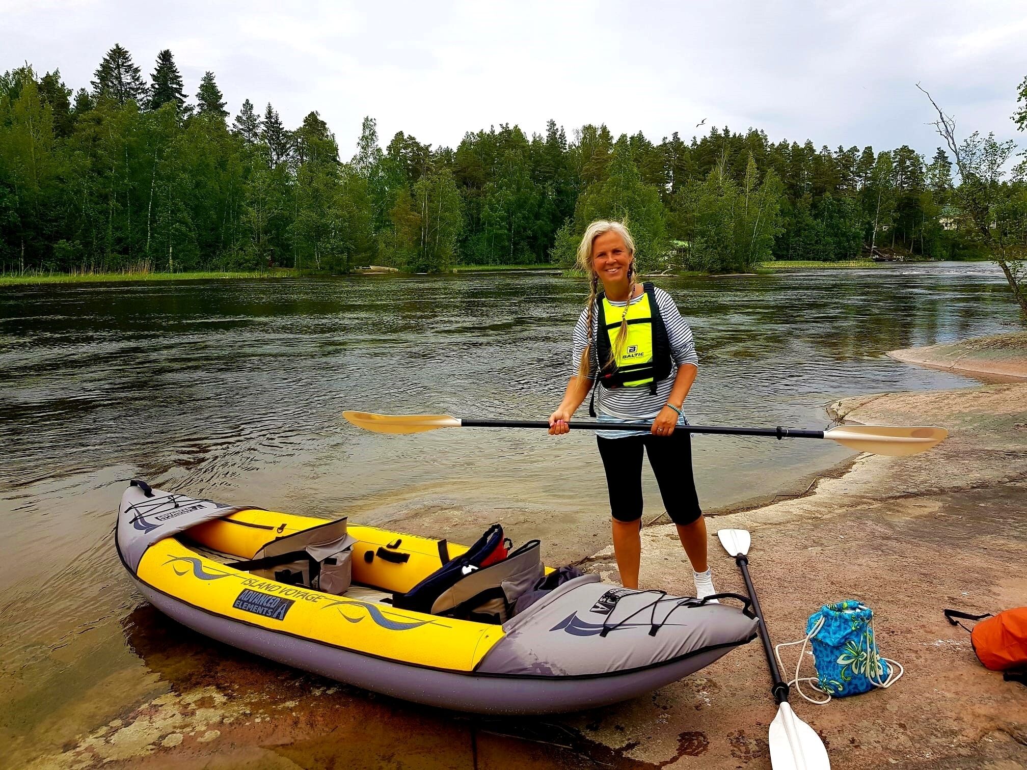 A person standing next to a yellow and gray kayak on a riverbank.