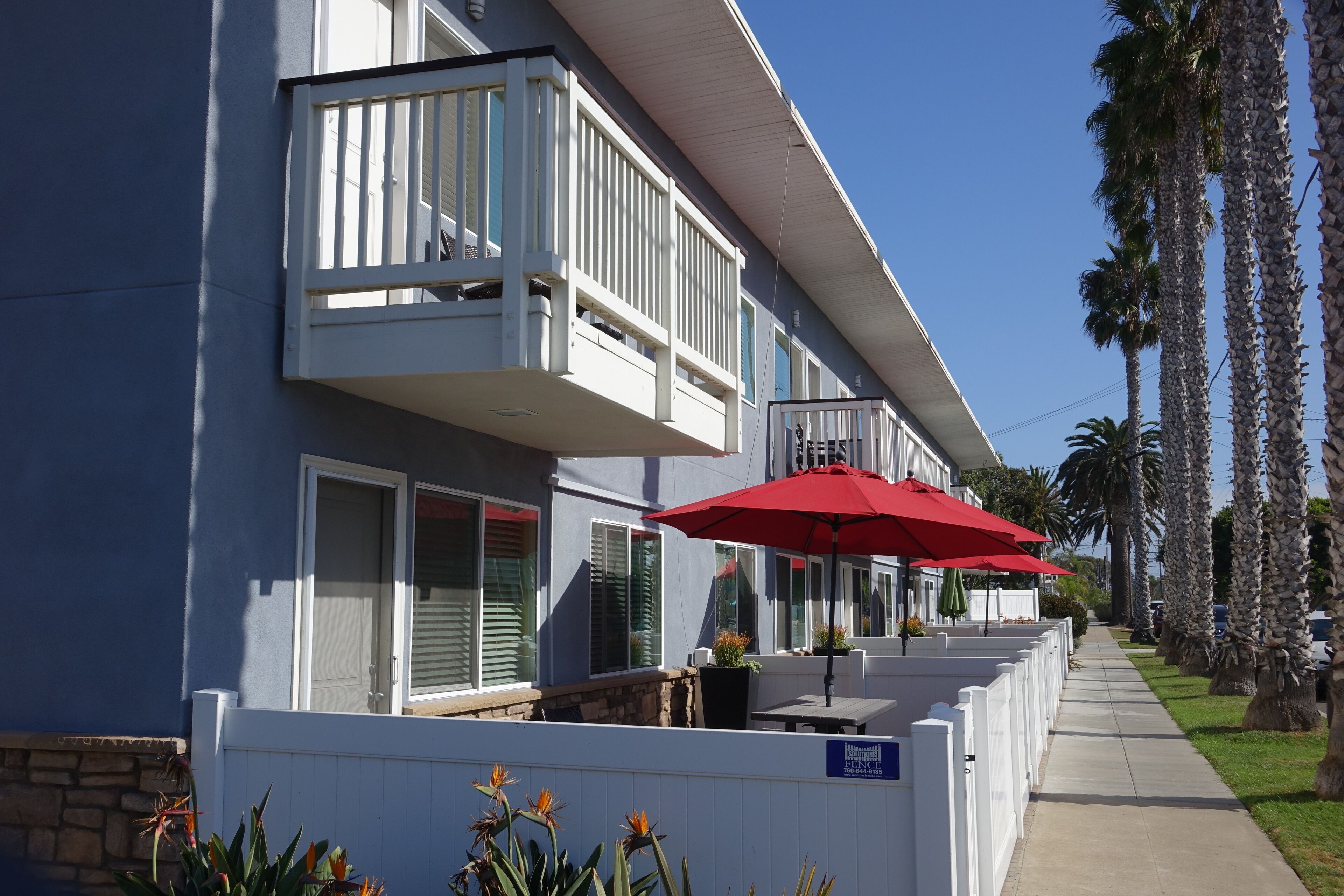 Un hotel con un balcone, arredi esterni e palme.