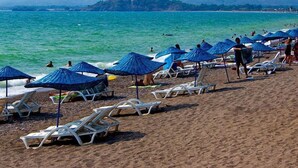 A beach with sun loungers and umbrellas, a clear view of the sea, and mountains in the background. - Sea Heaven Legend Apartments (Fethiye)