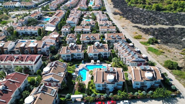 A coastal residential area with rows of houses, a central swimming pool, and a rocky shoreline. - Sea Heaven Legend Apartments (Fethiye)