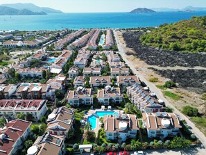 A coastal residential area with rows of houses, a central swimming pool, and a rocky shoreline. - Sea Heaven Legend Apartments (Fethiye)