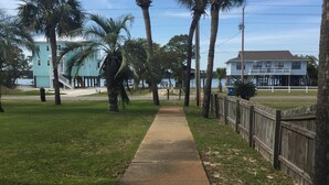 A coastal walkway lined with palm trees, leading to a beach area with a wooden fence and a building with a balcony overlooking the water. - GULF VILLAGE CONDO LOCATED ON THE BEACH, DIRECT VIEW OF THE GULF, Sleeps 4. (Gulf Shores)