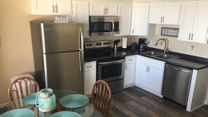 A compact kitchen with white cabinets, stainless steel appliances, and a dining area with a glass table and chairs. - GULF VILLAGE CONDO LOCATED ON THE BEACH, DIRECT VIEW OF THE GULF, Sleeps 4. (Gulf Shores)