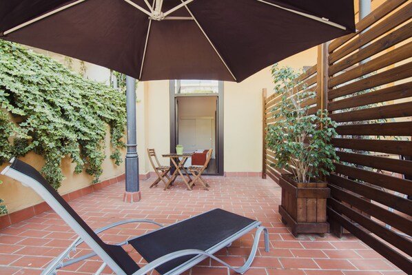 Un patio con una silla de descanso, una mesa y una planta en maceta.