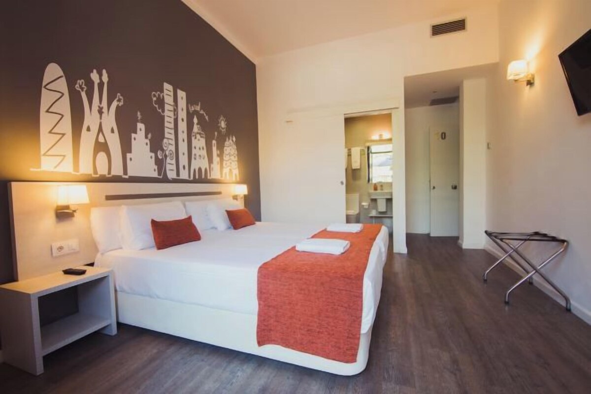 A hotel room with a large bed, a nightstand, a wall mural, and a bathroom visible through an open door.