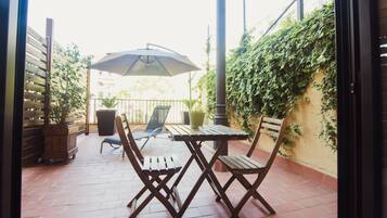 Une terrasse extérieure avec une table et des chaises en bois, un grand parasol et une plante en pot.