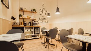 A cafe with wooden flooring, black chairs, and tables with menus. There are shelves with jars and a coffee machine. A wall sign reads "KEEP CALM AND DRINK COFFEE." - Hostal Live Barcelona (Barcelona)