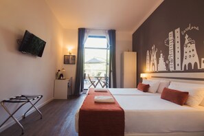 Habitación de hotel con cama, televisión montada en la pared, escritorio con silla y vistas a la ciudad por la ventana.