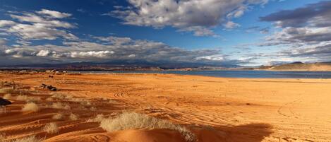 Paisaje desértico con dunas de arena y una masa de agua distante bajo un cielo parcialmente nublado.