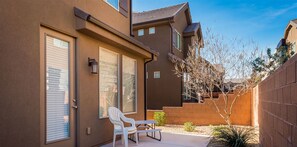 A residential building with a patio area featuring a white chair and table, a small garden, and a wooden fence.