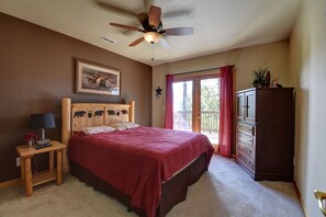 Um quarto com uma cama, uma mesa de cabeceira de madeira com abajur, um ventilador de teto, uma janela com cortinas e um armário de madeira.