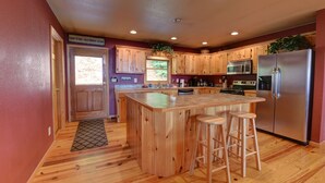 Cucina con mobili in legno, frigorifero in acciaio inossidabile e isola con sgabelli.
