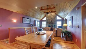 Un'ampia sala da pranzo con un tavolo e sedie in legno, un camino in pietra e un alto soffitto di legno.