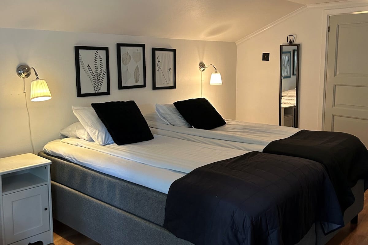 A bedroom with two beds, a nightstand, and wall-mounted lamps.