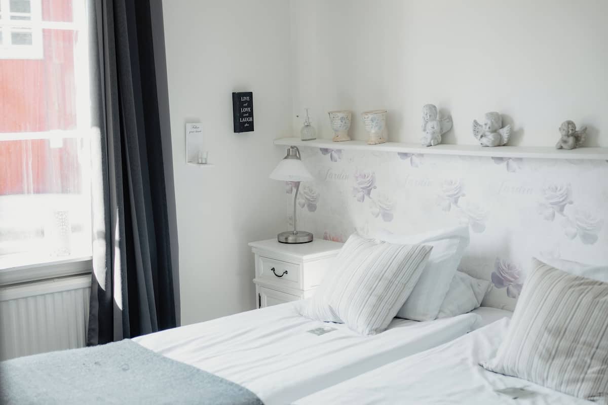A bedroom with two beds, a nightstand, a lamp, and a shelf with decorative items.