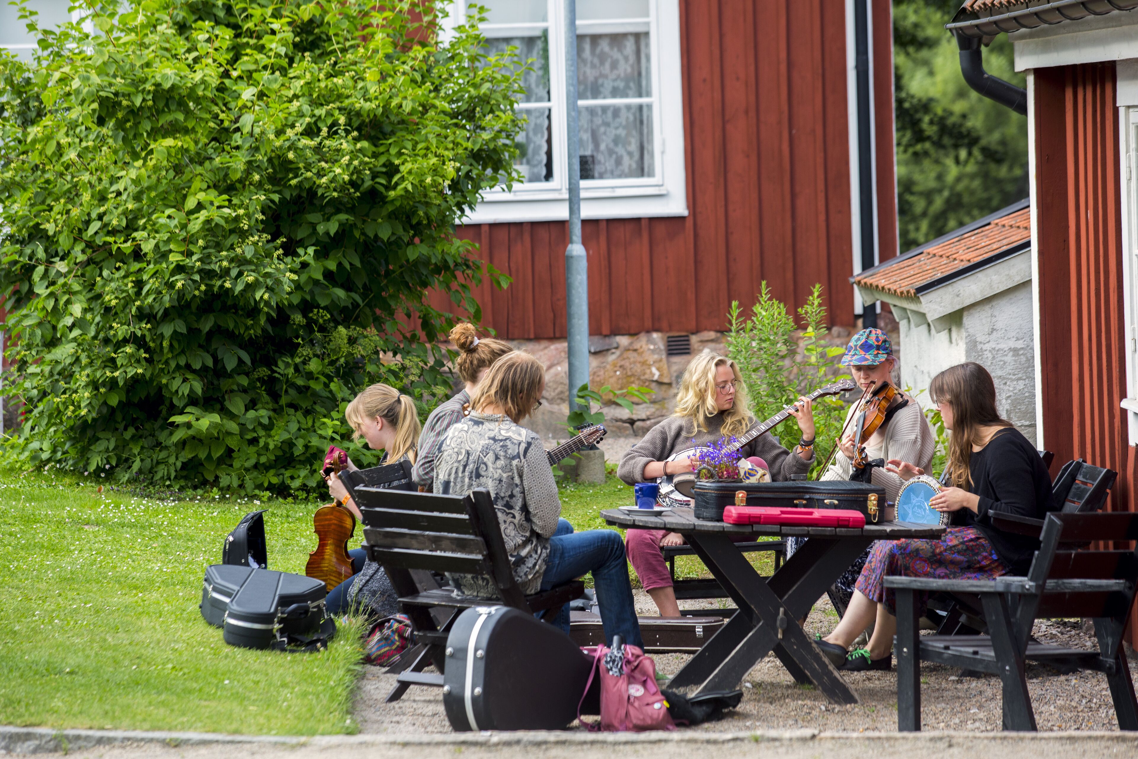 A group of people sitting outdoors with musical instruments, suggesting a casual outdoor music session.
