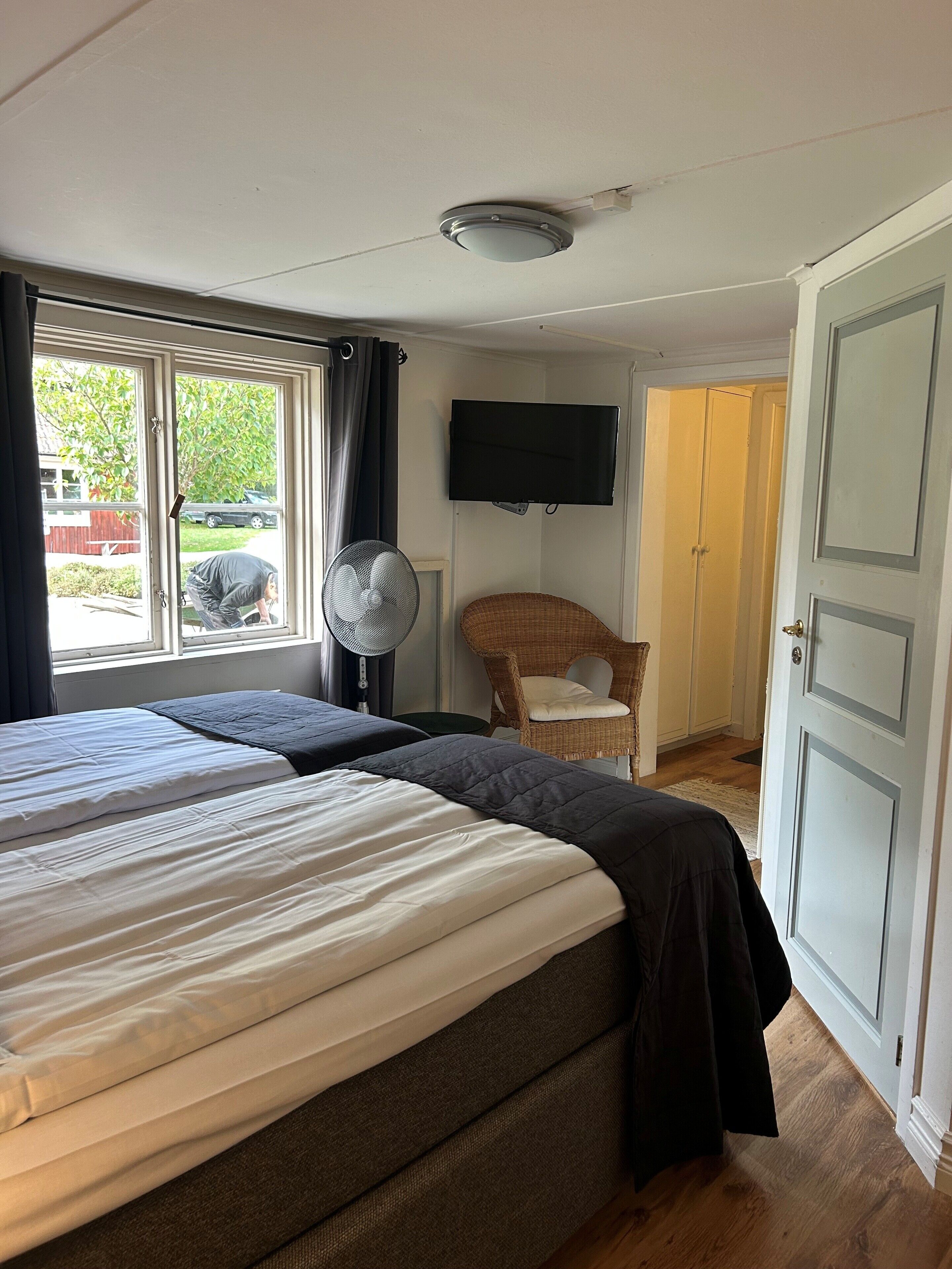 A hotel room with two beds, a TV mounted on the wall, a fan, and a wicker chair.