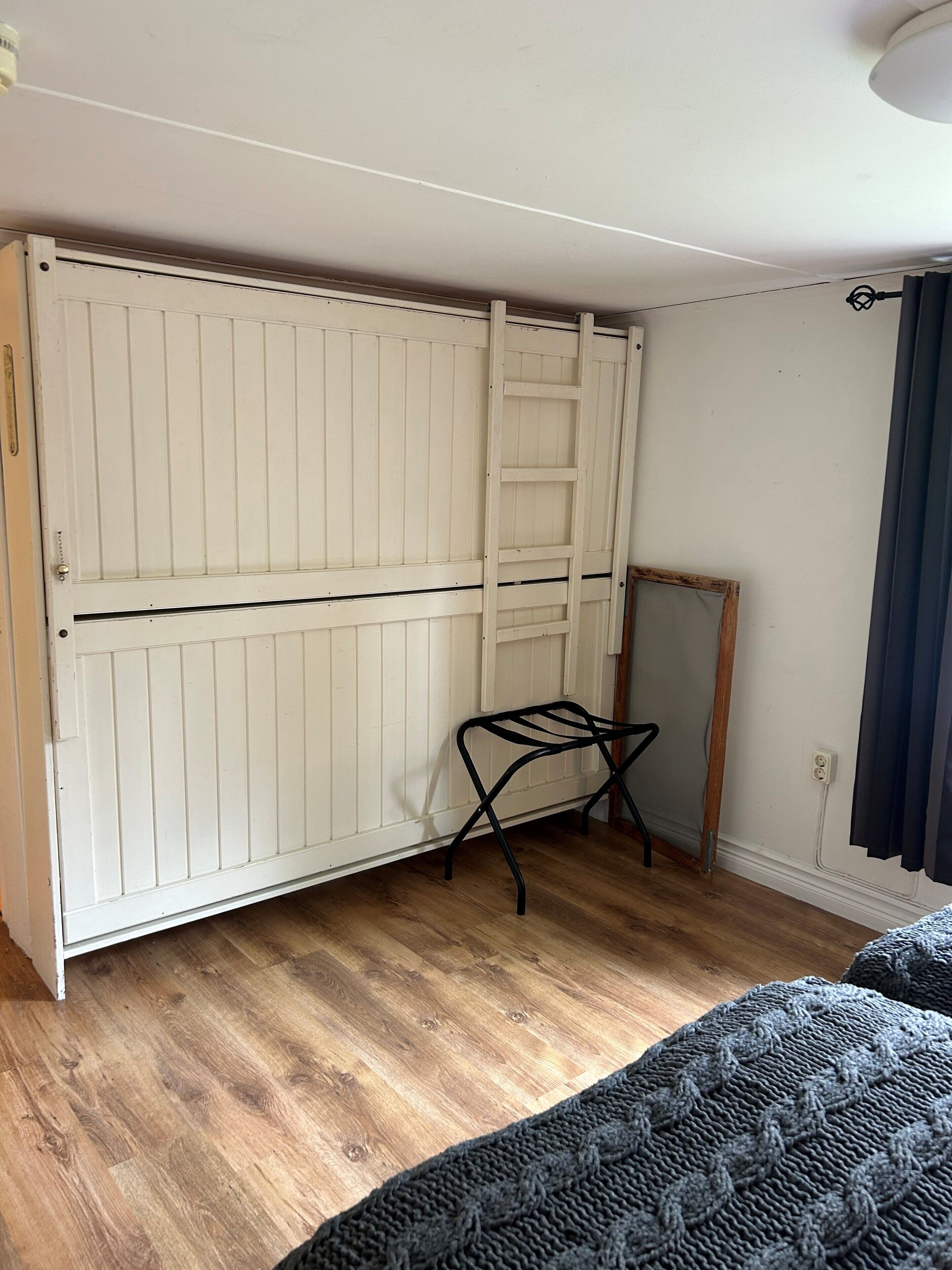 Una habitación con un armario blanco, un taburete de metal negro y suelo de madera.