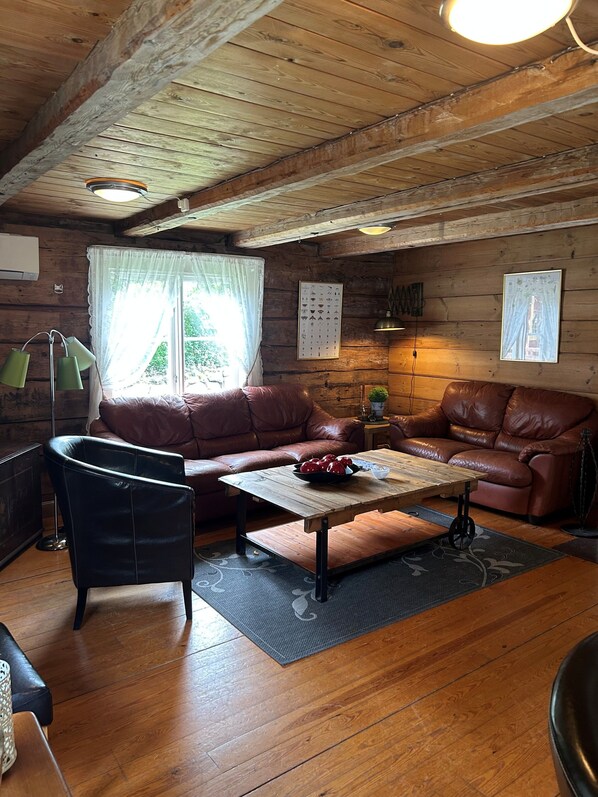 A cozy cabin interior with a wooden ceiling, a brown leather sofa, a black leather armchair, and a wooden coffee table. - Korrö Vandrarhem (Linneryd)