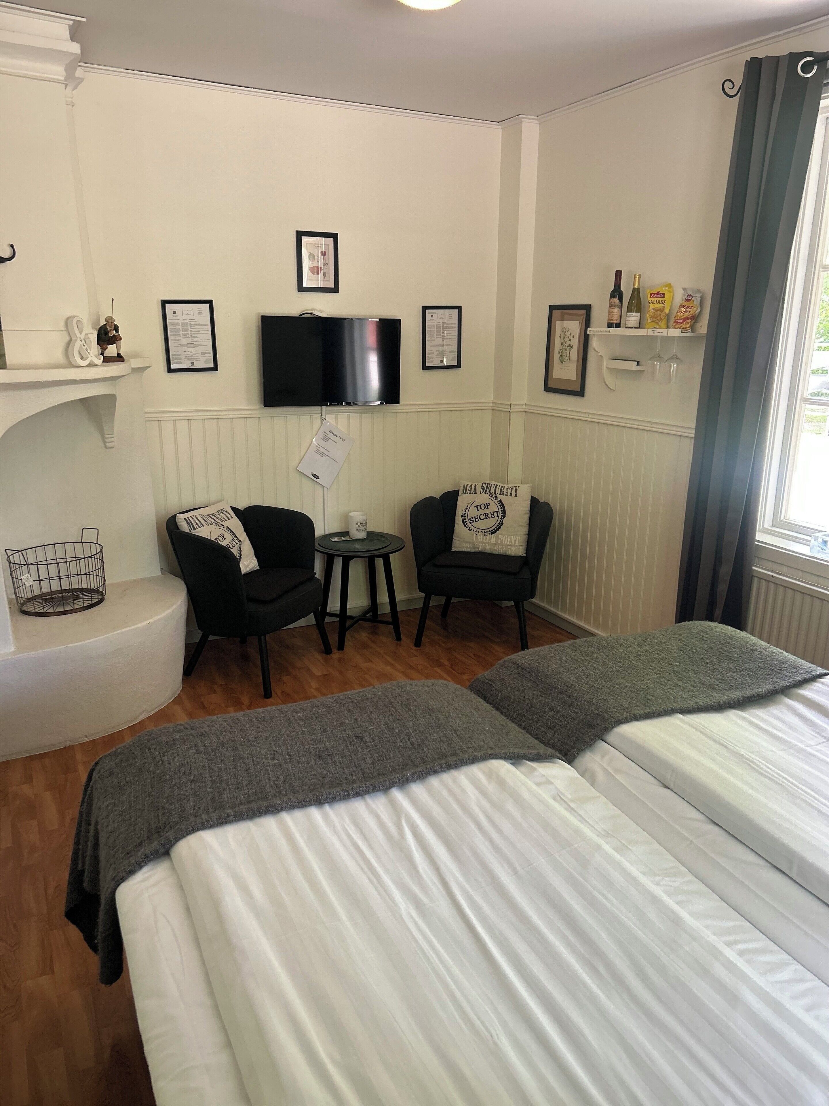 A hotel room with two beds, a television, a small table, two chairs, and a shelf with items.