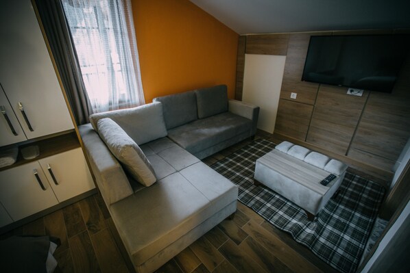 Un espacio habitable compacto con sofá, una mesita, televisor montado en la pared y un armario.