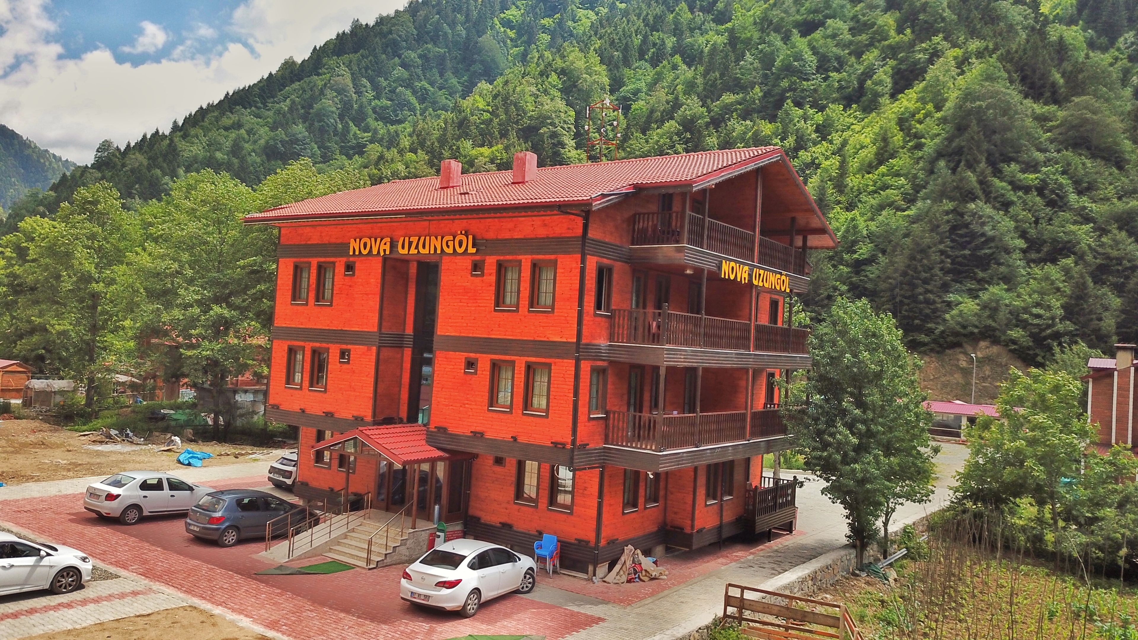 A multi-story building with balconies, labeled "NOVA UZUNGOL," surrounded by a forested area.