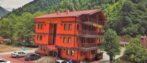 A multi-story building with balconies, labeled "NOVA UZUNGOL," surrounded by a forested area.