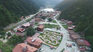 An aerial view of a town with a central square, surrounded by buildings with red roofs, a road, and a body of water in the distance.