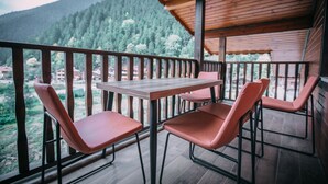A wooden deck with a table and four chairs, overlooking a forested valley.