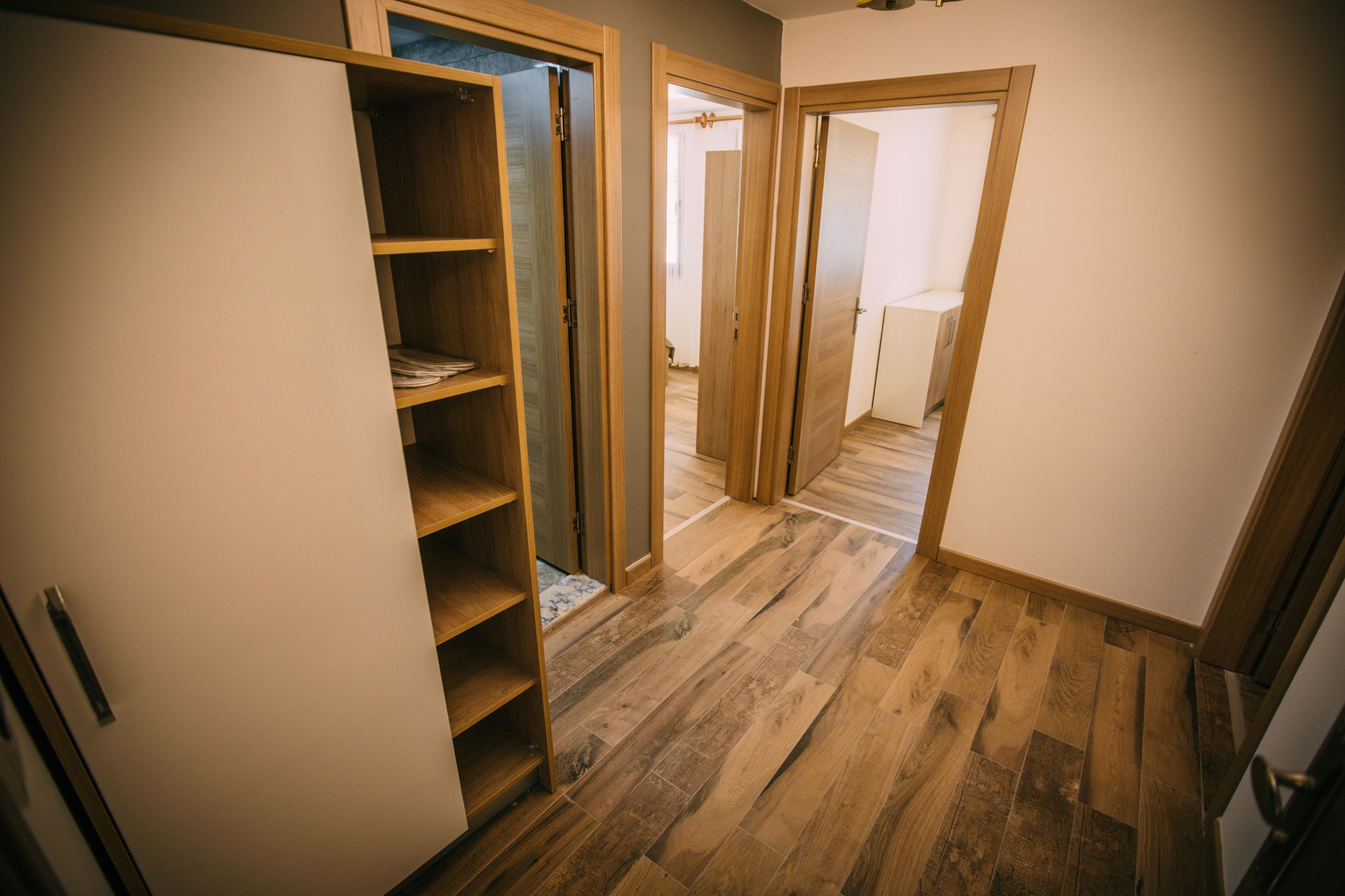 Un couloir doté d’un plancher en bois, d’un placard intégré avec des étagères et d’une porte donnant sur une autre pièce.