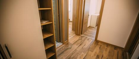 Un couloir doté d’un plancher en bois, d’un placard intégré avec des étagères et d’une porte donnant sur une autre pièce.