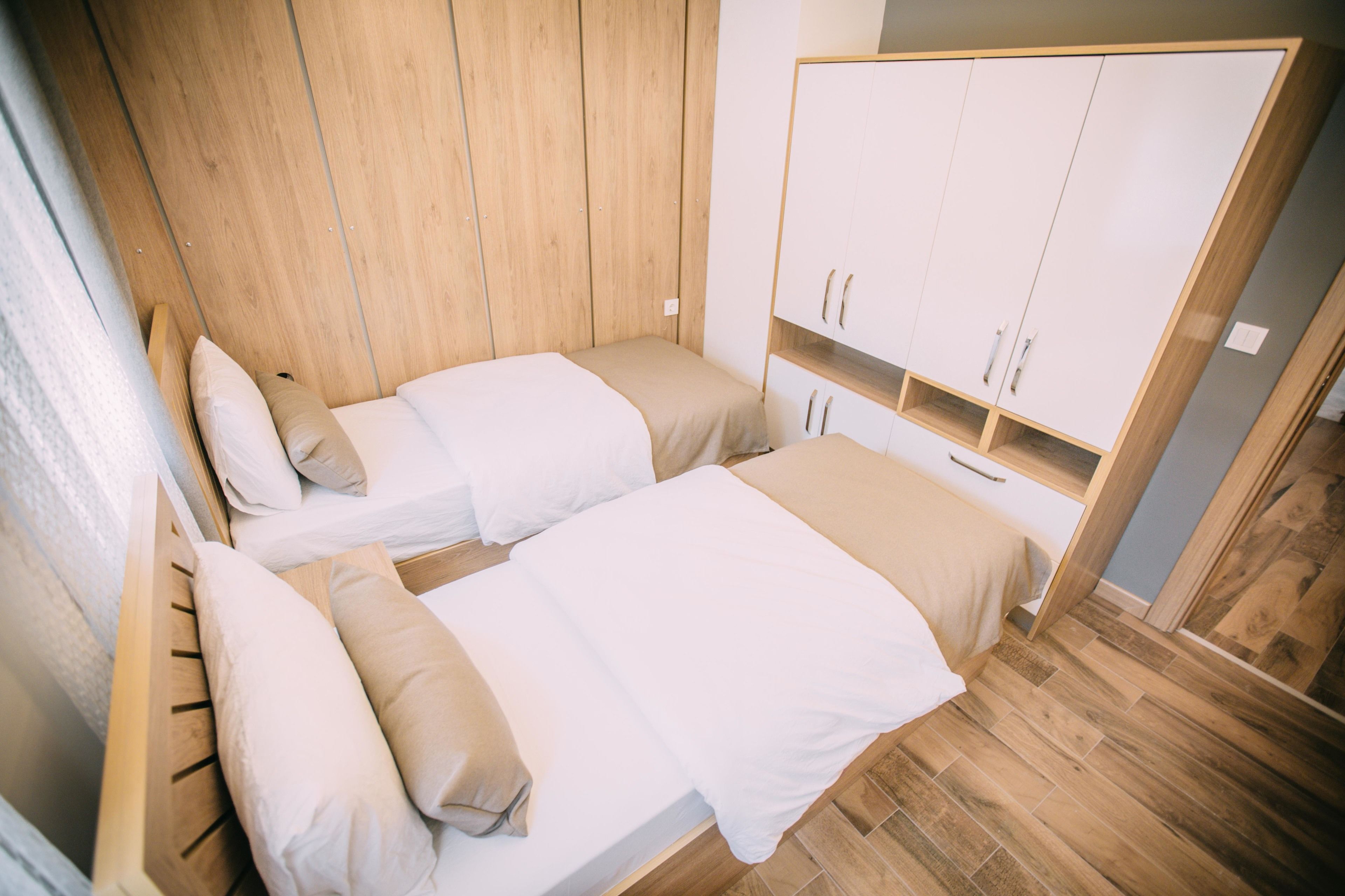 A bedroom with two beds, wooden wardrobe, and a wooden floor.