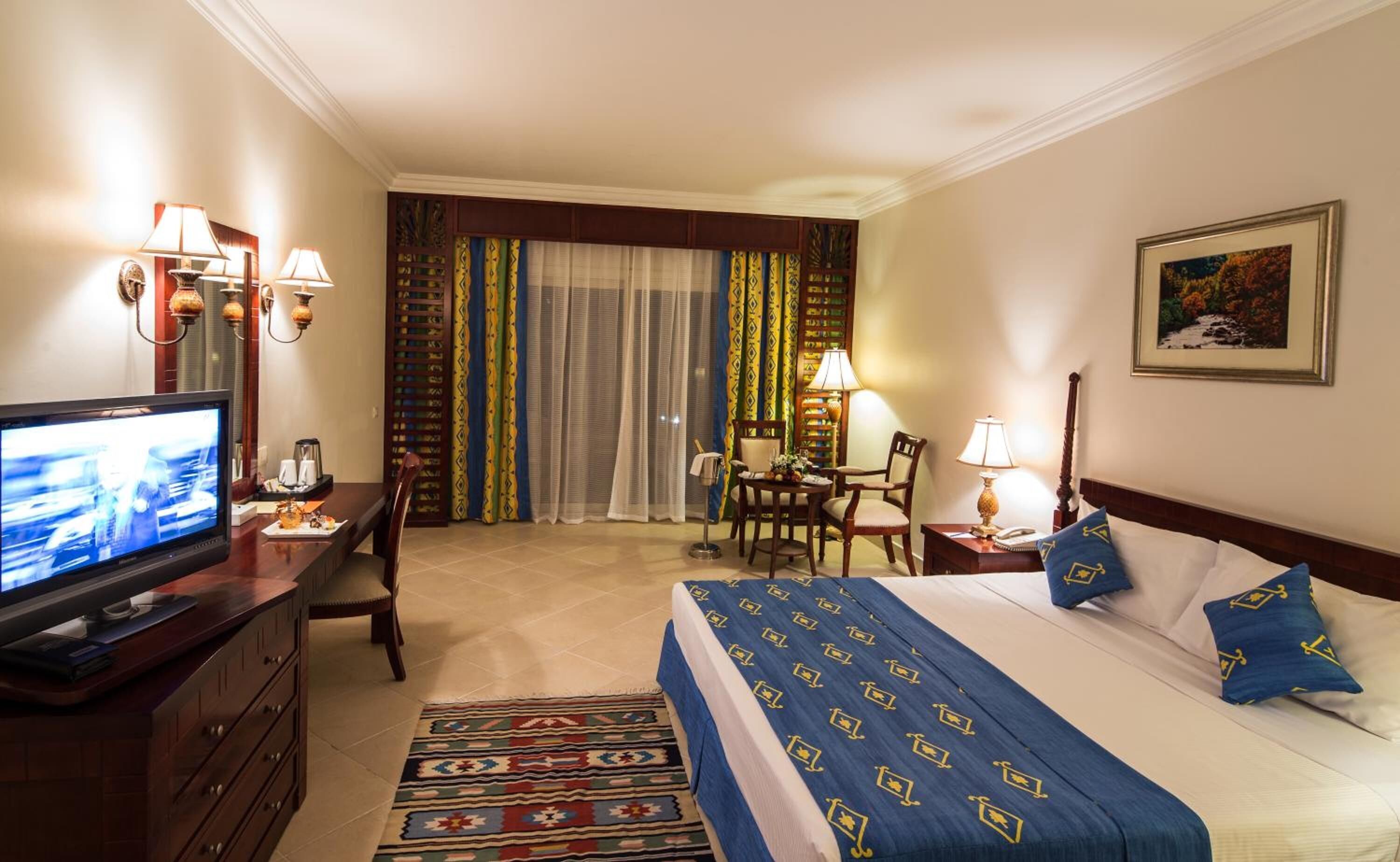Une chambre d’hôtel comprenant un lit, un bureau, une télévision et un coin repas agrémenté de rideaux.