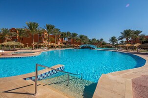 Ein großer Swimmingpool mit einer Brücke, Palmen und Resortgebäuden im Hintergrund.