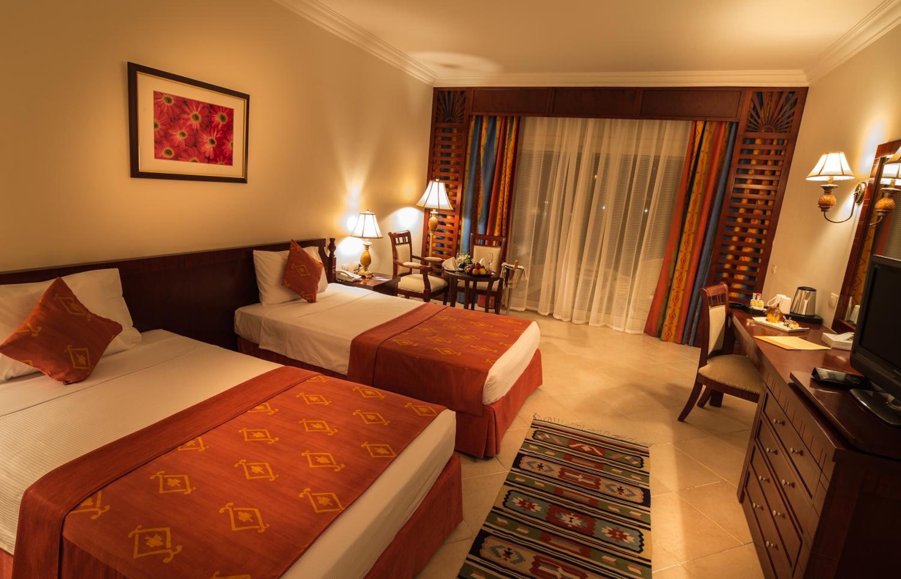 A hotel room with two beds, a desk with a chair, a television, and a window with curtains.