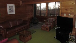 Een gezellig, chalet-achtig ingerichte kamer met een leren bank, een kleine houten tafel, een gestreept fauteuil en een televisie.