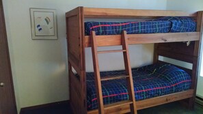 Una cama litera con escalera de madera, un cuadro en la pared y una colcha estampada.