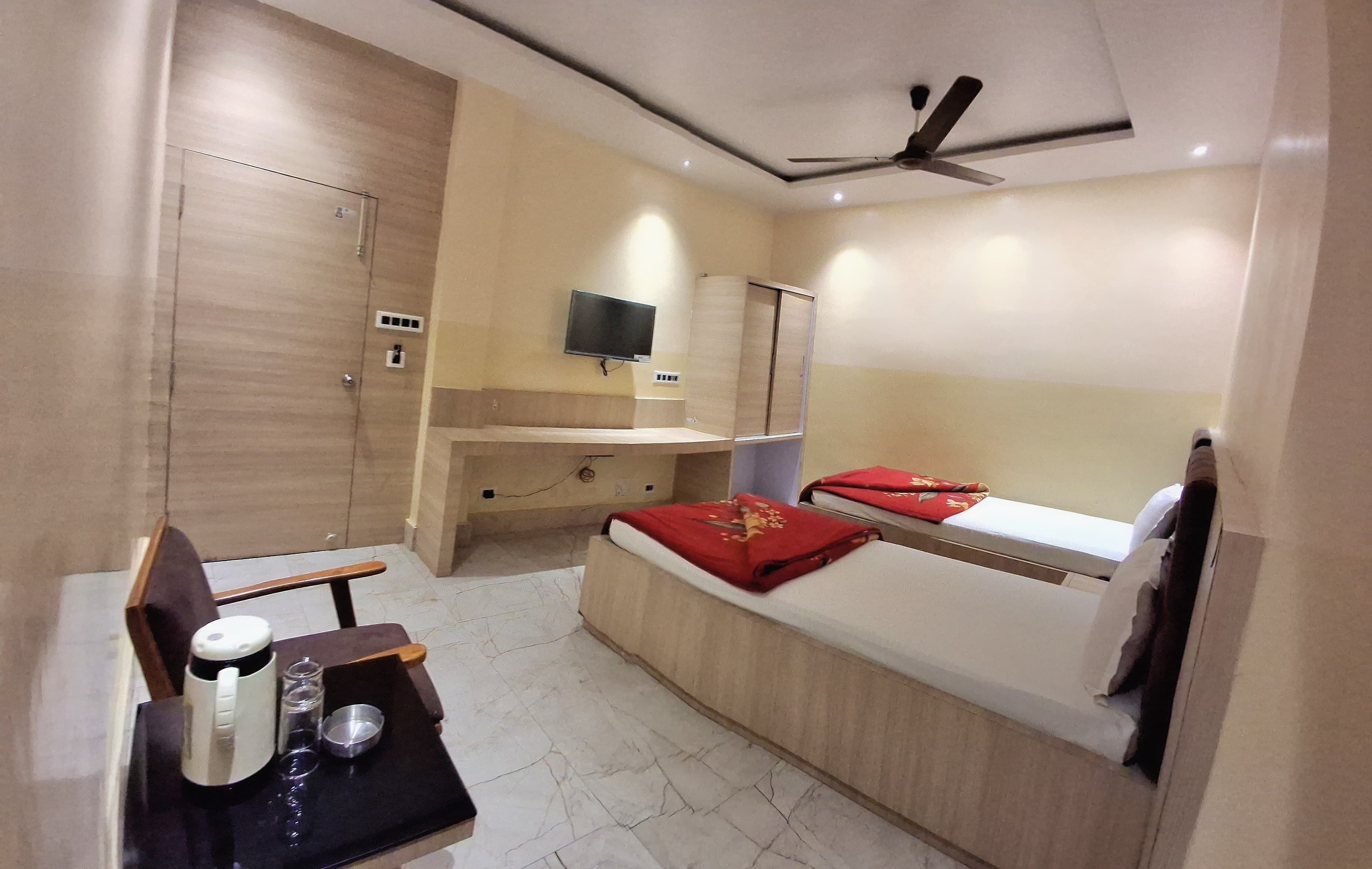 Una habitación de hotel compacta con cama, un pequeño escritorio con silla, un televisor montado en la pared y un ventilador de techo.