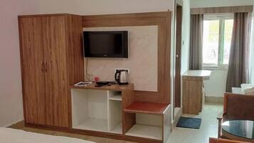 Habitació d'hotel amb armari de fusta, televisió penjada a la paret, taula petita amb una tetera i finestra amb cortines.