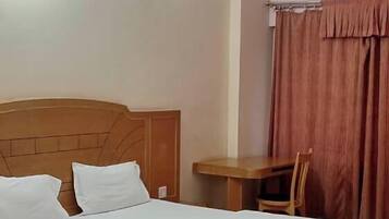 Habitación de hotel con cama, una mesa, una silla, ventilador de techo y luz empotrada en la pared.