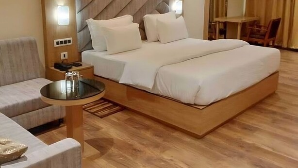 Quarto de hotel moderno com uma cama grande, um espaço de estar com mesa e um ventilador de teto.