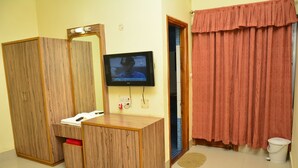 A room with a wooden vanity, a television mounted on the wall, a red curtain, and a small white trash bin. - Hotel Relax (Deoghar)