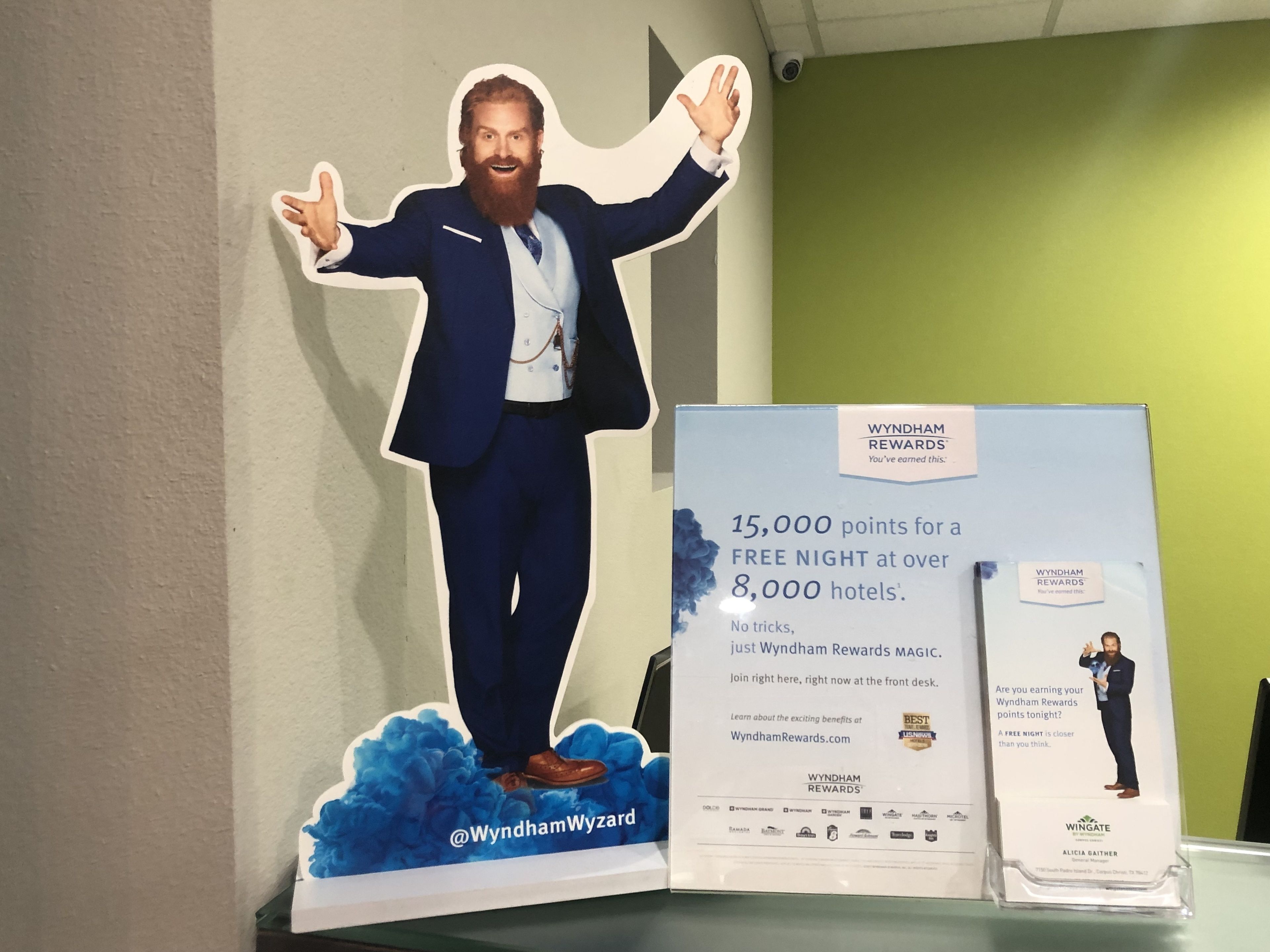Une présentation promotionnelle pour le programme de fidélité Wyndham Rewards, comprenant une découpe représentant un homme en costume, les bras tendus, une brochure et une petite carte.