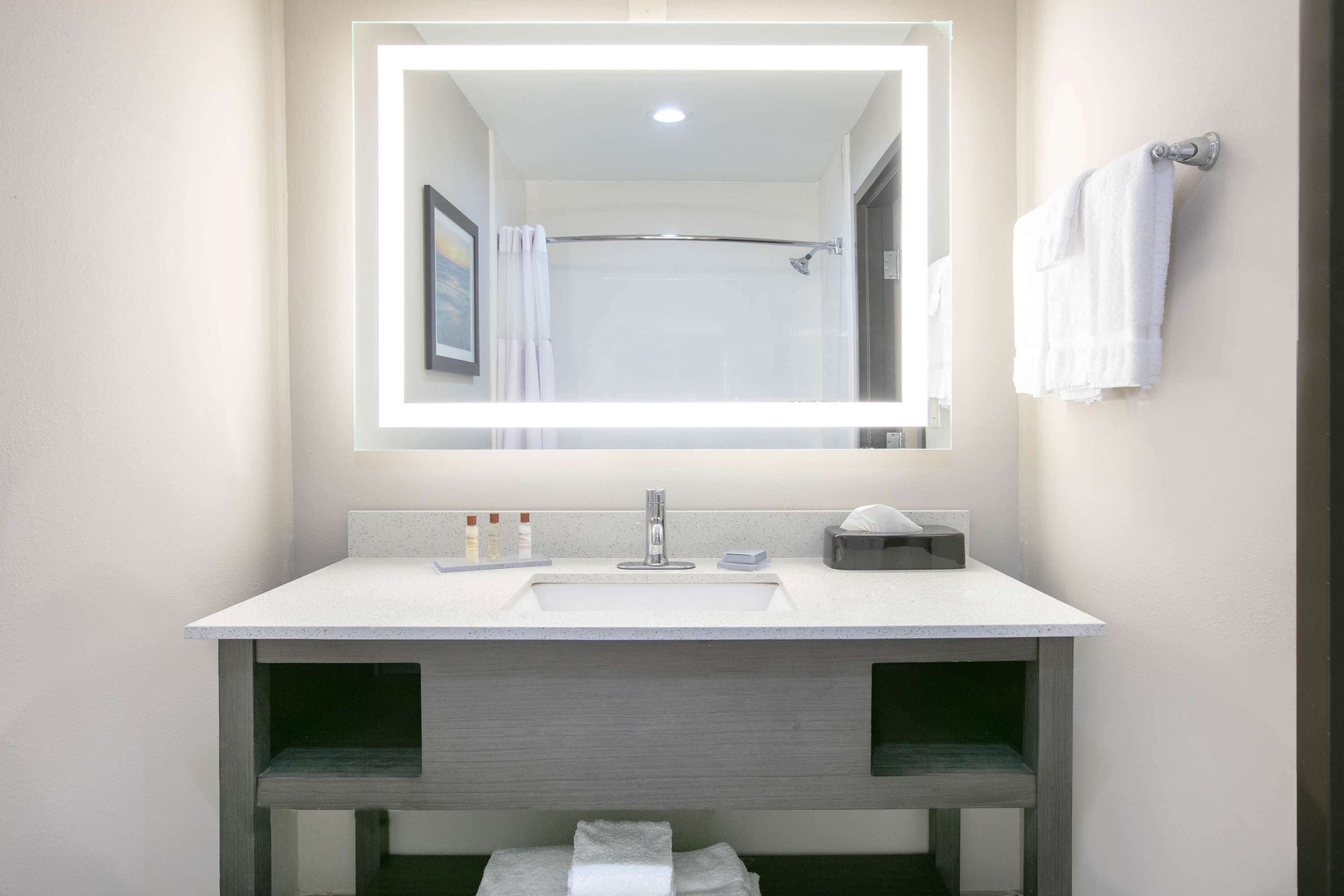 A modern bathroom with a large mirror, a sink, and a shower.