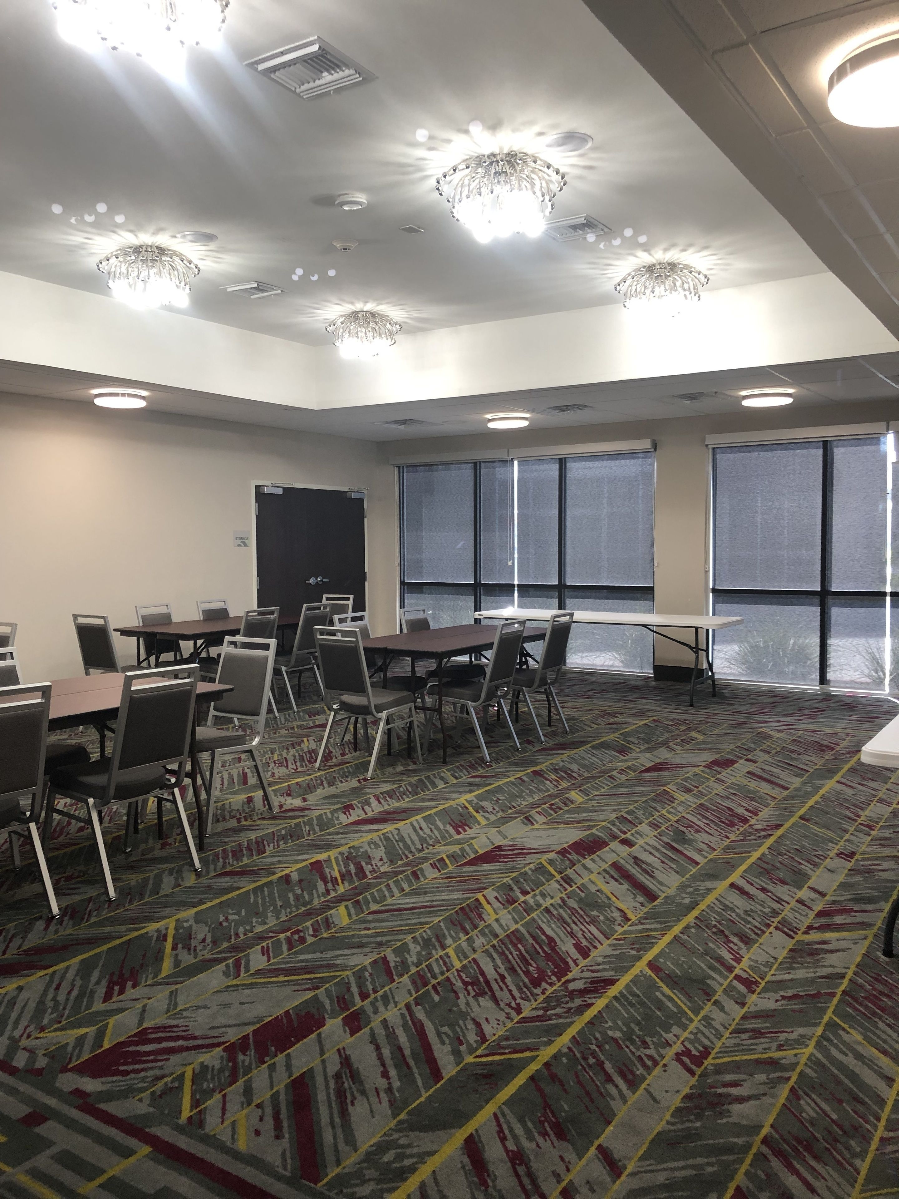 Une salle de conférence équipée de tables et de chaises, de grandes fenêtres et de luminaires au plafond.