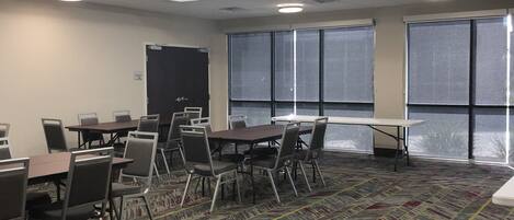 Une salle de conférence équipée de tables et de chaises, de grandes fenêtres et de luminaires au plafond.